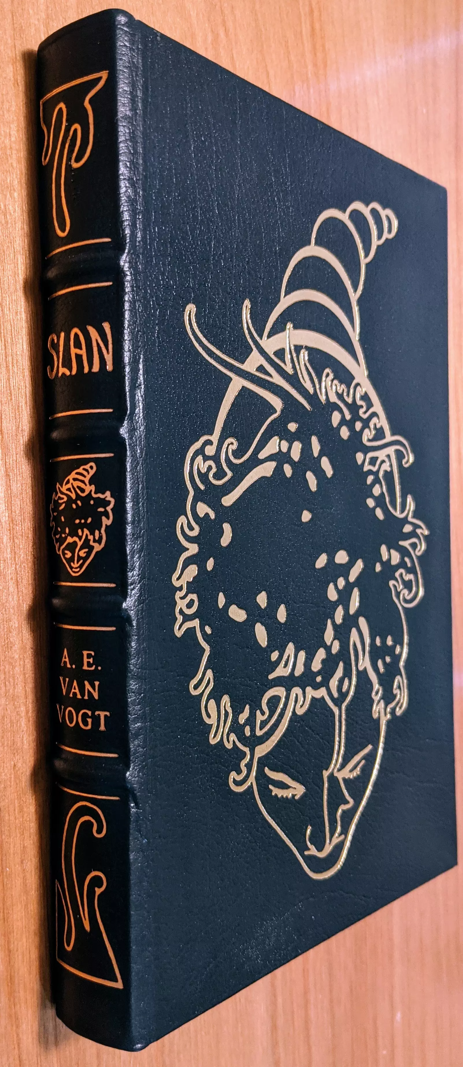 This is a pristine, leather-bound Collector’s Edition of Slan by A. E. van Vogt, published by The Easton Press as part of the Masterpieces of Science Fiction Collection. Bound in dark green leather with hubbed spines, the book is accented in 22kt gold. The front cover features an intricate gold-embossed illustration of a stylized face with tendrils of hair that morph into curved, organic shapes, evoking an otherworldly or telepathic essence. The spine bears gold lettering displaying the title SLAN and the author's name, A. E. van Vogt, accompanied by two ornate symbols, one at the top and one at the bottom, reinforcing the book’s elegant design.
 -
The pages are printed on archival-quality, acid-neutral paper, ensuring longevity and preservation. The page edges are gilded, creating a radiant gold shimmer when viewed from the side. Inside, the book includes a pristine bookplate and features an original frontispiece artwork by Richard Powers. This edition is personally signed by the author, with a dedicated signature page confirming its authenticity. The smyth-sewn binding ensures durability, while concealed muslin joints provide additional structural integrity.
 - 
Meticulously preserved in a dust-free bookcase within a dry climate by a single private owner, this volume remains in pristine condition.
 - 
A stunning and rare collectible for science fiction enthusiasts and fine book collectors alike.