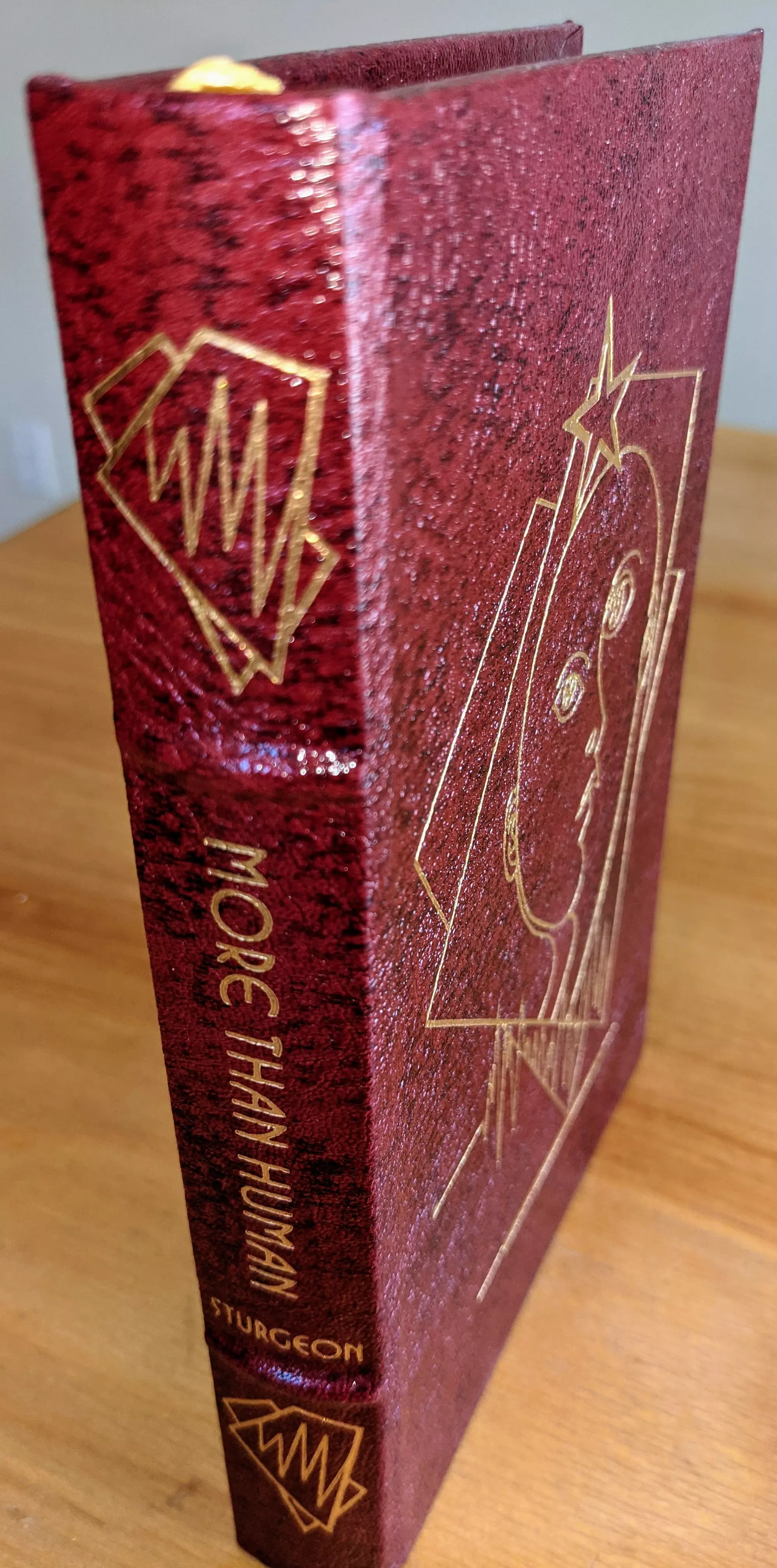 This is a pristine, leather-bound Collector’s Edition of More Than Human by Theodore Sturgeon, published by The Easton Press in 1994 as part of the Masterpieces of Science Fiction Collection. Winner of the 1954 International Fantasy Award. Bound in stunning dark maroon speckled leather with hubbed spines, the book is accented in 22kt gold. Introduction by two-time Nebula award winning author Michael Bishop
 - 
The front cover displays a stylized geometric design incorporating a human face and a star, capturing the essence of the book’s thought-provoking themes. The spine is adorned with the title More Than Human in bold gold serif font, with the author’s name, Sturgeon, at the base. Angular, lightning-like gold accents further enhance the spine’s design
 -
The pages are printed on archival-quality, acid-neutral paper, ensuring longevity and preservation. The page edges are gilded, creating a radiant gold shimmer when viewed from the side. Inside, the book includes a pristine bookplate and features an original frontispiece artwork by Jeff Fisher. The smyth-sewn binding ensures durability, while concealed muslin joints provide additional structural integrity
 - 
Meticulously preserved in a dust-free bookcase within a dry climate by a single private owner, this volume remains in pristine condition
 - 
A stunning and rare collectible for science fiction enthusiasts and fine book collectors alike
