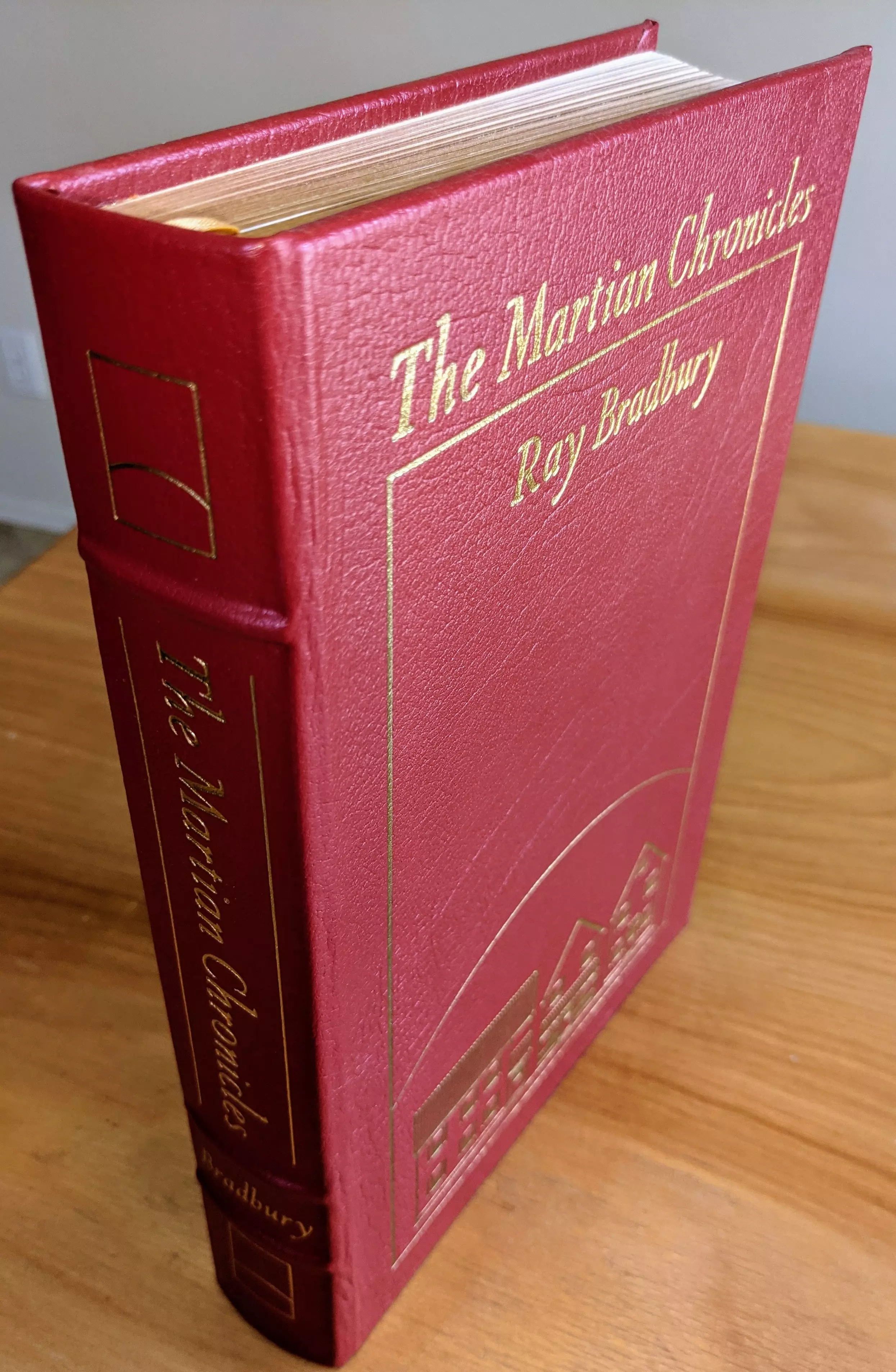 SIGNED Collector's Edition of The Martian Chronicles by Ray Bradbury is an elegantly bound volume meticulously preserved in pristine condition. Part of a private, single-owner collection, it has been carefully stored in dust-free bookcases within a dry climate to maintain its flawless quality. The book is bound entirely in luxurious, deep crimson leather, accented beautifully in lustrous 22kt gold detailing. The front cover features the title, The Martian Chronicles, and author Ray Bradbury prominently embossed in gold script at the top.
 - 
Original artwork by renowned illustrator Joseph Mugnaini adorns the cover, carefully rendered in subtle gold lines beneath the title. This minimalist yet evocative illustration suggests Martian architectural structures, capturing the novel's imaginative and reflective spirit. The spine, richly hubbed and elegantly designed, prominently displays the title and author's last name in complementary gold lettering, accompanied by tasteful decorative accents. Introduction by Damon Knight.
 - 
This limited-run edition is personally signed by Ray Bradbury. Produced by The Easton Press for their esteemed Masterpieces of Science Fiction Collection, it features archival-quality paper, gilded page edges that shimmer gently, traditional smyth-sewn binding, and concealed muslin joints ensuring longevity. Inside the front cover is an immaculate, unused bookplate, confirming its condition as pristine, unread, and carefully preserved.