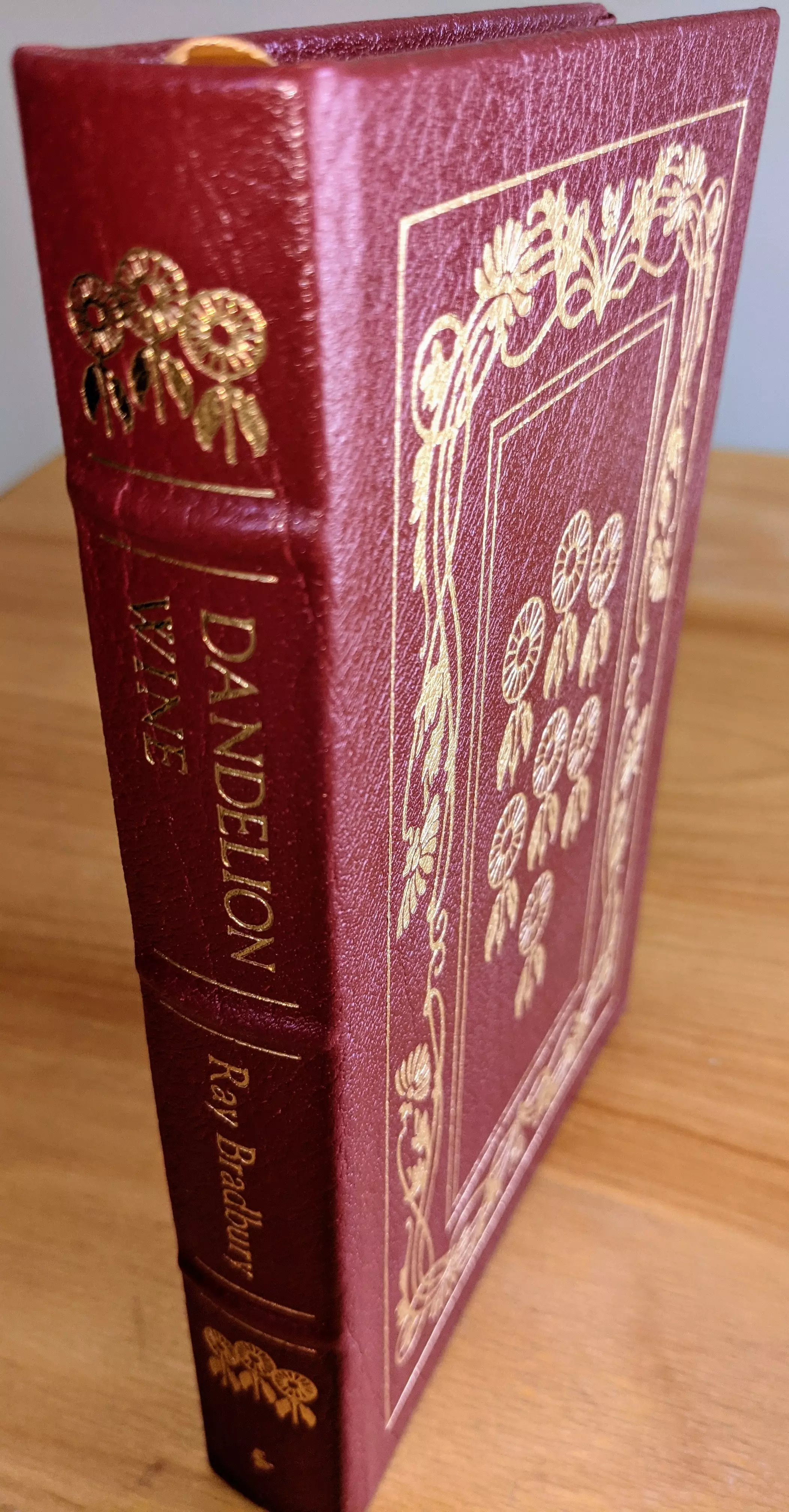 Breathtaking maroon leather-bound edition of Dandelion Wine by Ray Bradbury, from the Masterpieces of Science Fiction Collection by The Easton Press. This collector's edition is a limited run, exquisitely designed with intricate gold-embossed artwork. The front cover is adorned with delicate floral patterns, specifically dandelions rendered in 22kt gold, with a rectangular frame accentuating the centerpiece. The spine displays the title Dandelion Wine in bold gold lettering, alongside the author's name, Ray Bradbury, and features additional gold motifs of dandelions
 - 
Bound in full leather with raised hubbed spines, this volume combines durability and elegance, showcasing the exceptional craftsmanship characteristic of Easton Press editions. Printed on high-quality acid-neutral archival paper with 22k gold gilded edges. The binding features smyth-sewn construction and concealed muslin joints
 - 
This pristine edition is part of a single-owner private collection, carefully stored unread in dust-free bookcases within a dry climate to maintain its flawless condition. A pristine bookplate is included on the inside of the front cover
 - 
Additionally, the volume features original artwork by Joseph Mugnaini, whose iconic illustrations perfectly complement Bradbury's evocative prose, capturing the novel's nostalgic and poetic essence. This stunning edition is a masterpiece of literary and artistic excellence, a true treasure for collectors and admirers of Ray Bradbury's work