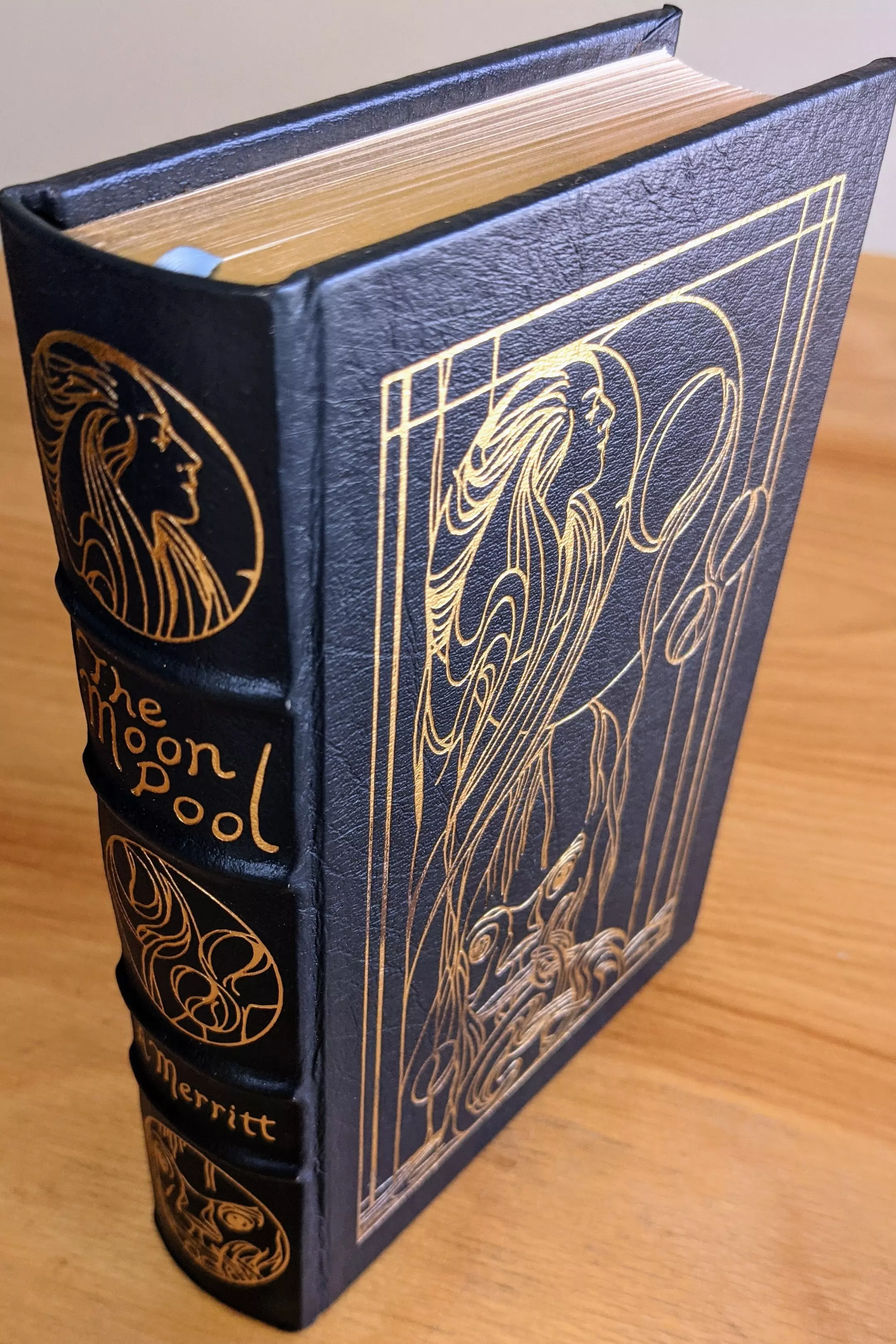 This is the Easton Press collector's edition of The Moon Pool by A. Merritt, part of the Masterpieces of Science Fiction collection. This volume is a limited-run, single-owner item from a private collection, stored in dust-free bookcases in a dry climate to ensure long-term preservation. The book is bound in full, deep navy blue leather with hubbed spines and features elaborate original cover art by Todd Cameron Hamilton, rendered in 22kt gold leaf. The design is in the Art Nouveau style, with fluid, organic lines depicting a female figure and other fantastical elements. The spine bears the title The Moon Pool, the author's name Merritt, and two circular gold illustrations, all vertically aligned and embossed in 22k gold
 - 
The edition is printed on archival-quality, acid-neutral paper with 22k gold gilded edges and features smyth-sewn binding and concealed muslin joints for durability and refined finish. A pristine Easton Press bookplate is affixed inside the front cover, untouched and unmarked. The book includes an introduction by noted science fiction scholar James Gunn, adding valuable context to this early work of speculative fiction
 - 
Condition is pristine overall, with the exception of a minor flaw in the gold leaf on the front cover's artwork, an imperfection that was present upon delivery from Easton Press. This volume exemplifies Easton Press's craftsmanship and commitment to producing heirloom-quality editions for discerning collectors