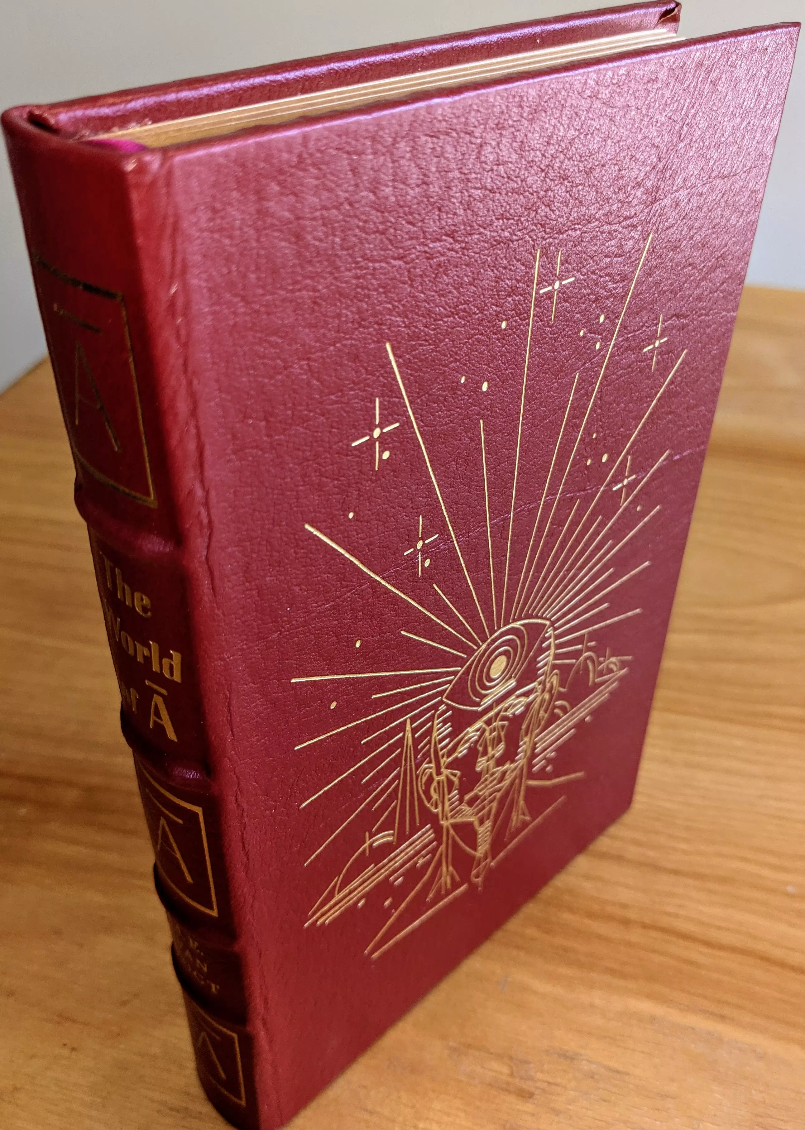 This is the collector's edition of The World of A by A.E. van Vogt, published by The Easton Press as part of its Masterpieces of Science Fiction series. The volume is bound in rich, full-grain red leather with hubbed spines and accented in genuine 22kt gold. 
 - 
The front cover features an intricate 22k gold-foil stamped illustration by Vincent Di Fate, original artwork unique to this limited run, depicting a stylized, abstract human head with a target-like pattern on the crown, set against a backdrop of geometric, futuristic landscapes and radiant lines that evoke cosmic energy. Surrounding the central figure are clusters of starbursts and fine dot work, reinforcing the science fiction theme
 - 
The spine bears the title The World of A in gold, with the stylized 'Null-A' character prominently repeated in 22k gold-embossed panels at both ends. Inside, the book includes a pristine bookplate affixed to the inside front cover. The volume is printed on archival-quality, acid-neutral paper with gilded page edges for long-term preservation. It features smyth-sewn binding with concealed muslin joints for durability and ease of opening. This edition also contains a special introduction by noted science fiction scholar James Gunn
 - 
This specific copy comes from a single-owner private collection, stored exclusively in dust-free bookcases within a dry climate, ensuring pristine condition. It is a stunning collector's piece, carefully preserved and impeccably maintained