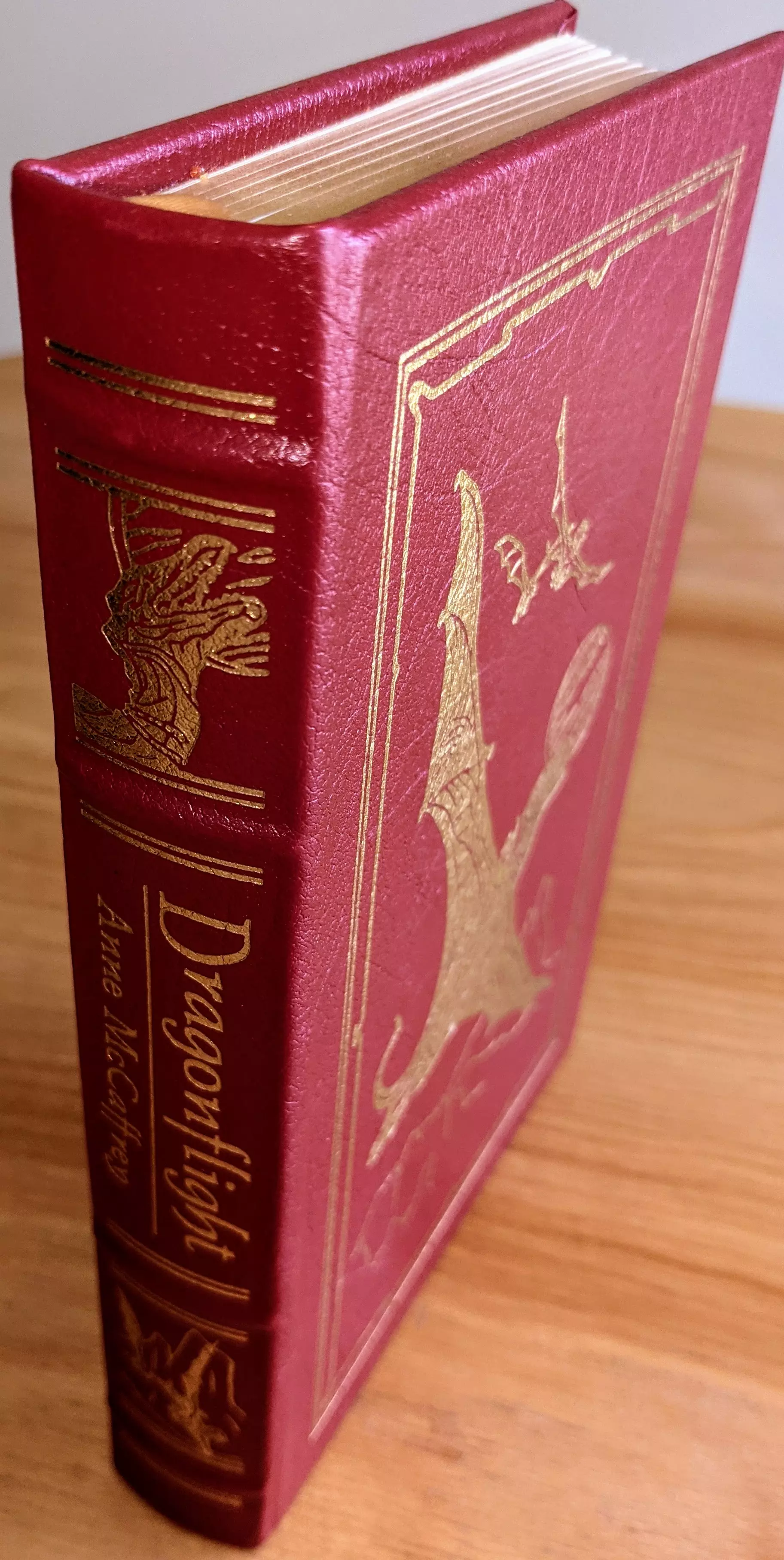 Stunning red leather-bound edition of Dragonflight by Anne McCaffrey, from the Masterpieces of Science Fiction Collection by The Easton Press. This collector's edition is a limited run, meticulously crafted to honor McCaffrey's iconic novel
 - 
The cover is adorned with 22kt gold-embossed artwork by Michael Whelan, featuring a dynamic depiction of a dragon in flight, accompanied by intricate detailing of a castle-like structure in the background. The scene is framed with elegant gold borders. The spine features the title in bold gold serif font, alongside the author's name. Additional design elements include a striking motif of mountains and dragons
 - 
This edition is bound in full leather with raised hubbed spines. The book is printed on archival-quality acid-neutral paper with 22k gold gilded edges, combining aesthetic brilliance with preservation. Smyth-sewn binding and concealed muslin joints provide flexibility and long-lasting structural integrity
 - 
Maintained in pristine condition, this book has been carefully stored unread in dust-free bookcases within a dry climate as part of a single-owner private collection. Inside the front cover is a pristine, untouched bookplate
 - 
This edition also features an introduction by Gordon R. Dickson, offering insightful context for McCaffrey's groundbreaking work. A masterpiece of literary craftsmanship and artistry, this volume is a perfect tribute to the rich world-building and enduring legacy of Dragonflight