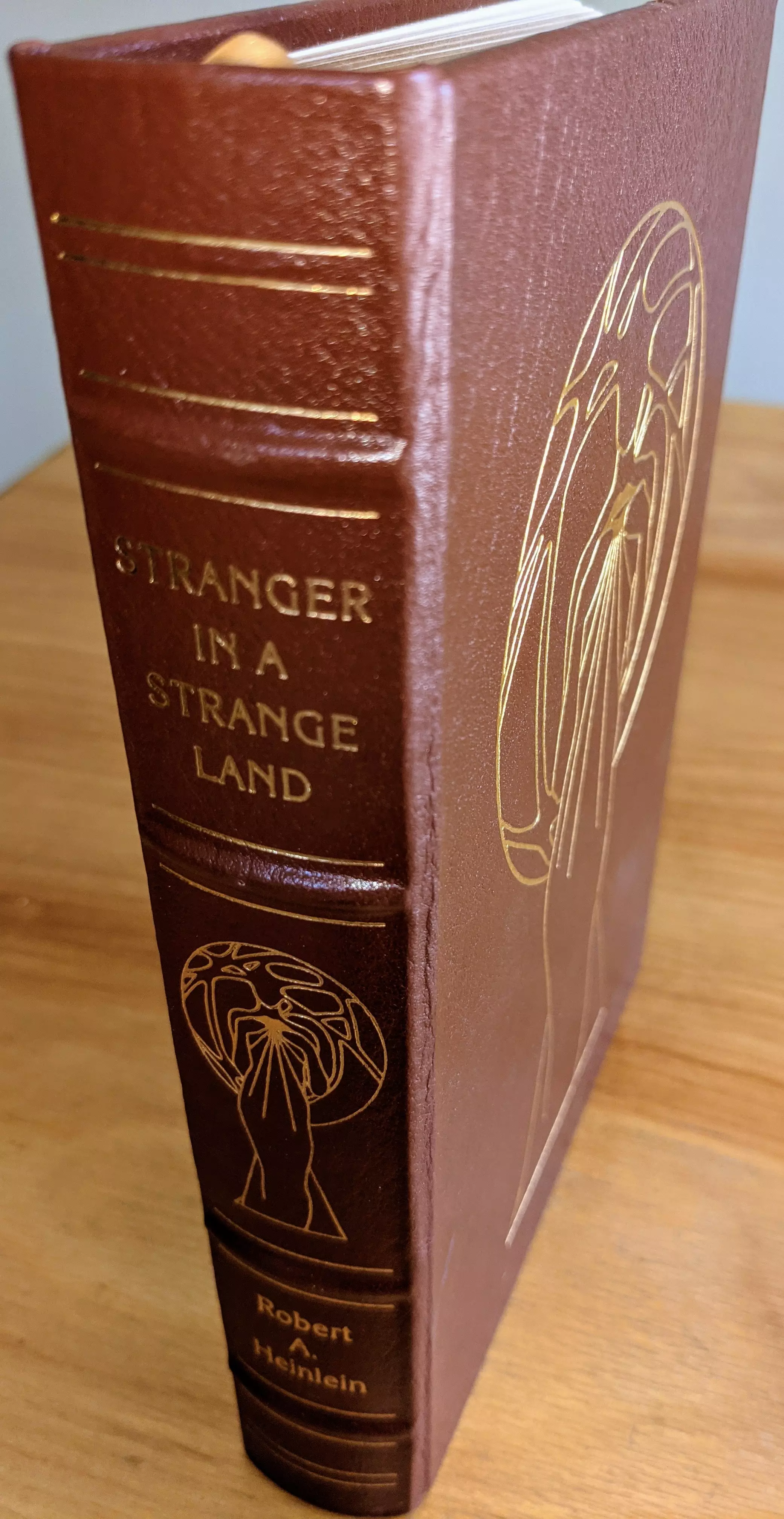 This is the Easton Press collector's edition of Stranger in a Strange Land by Robert A. Heinlein, issued as part of the Masterpieces of Science Fiction series. The book is bound in full brown leather with hubbed spines and accented in 22kt gold. The spine features four raised bands, gold-stamped title text reading STRANGER IN A STRANGE LAND, a stylized figure in gold, and the author's name, Robert A. Heinlein, at the base. Three parallel gold lines frame the upper, middle, and lower spine sections
 - 
The front cover features original artwork by Kent Bash, rendered in gold foil. The image depicts an abstract, elongated figure with raised arms, palms open and facing outward, surrounded by a circular, organic shape resembling an aura or energy field. The lines are minimalist but precise, emphasizing flow and symmetry in the posture. The same figure appears on the spine, matching the aesthetic of the front
 - 
This is the original full-length (uncut) edition, featuring a preface by Virginia Heinlein and an introduction by James Gunn. The volume is printed on archival-quality paper with gilded page edges. Smyth sewing and concealed muslin joints enhance durability. Includes a pristine bookplate affixed to the inside front cover
 - 
Condition is Pristine. Single-owner copy from a private collection, always stored in dust-free bookcases in a dry climate. A stunning, collector-grade volume