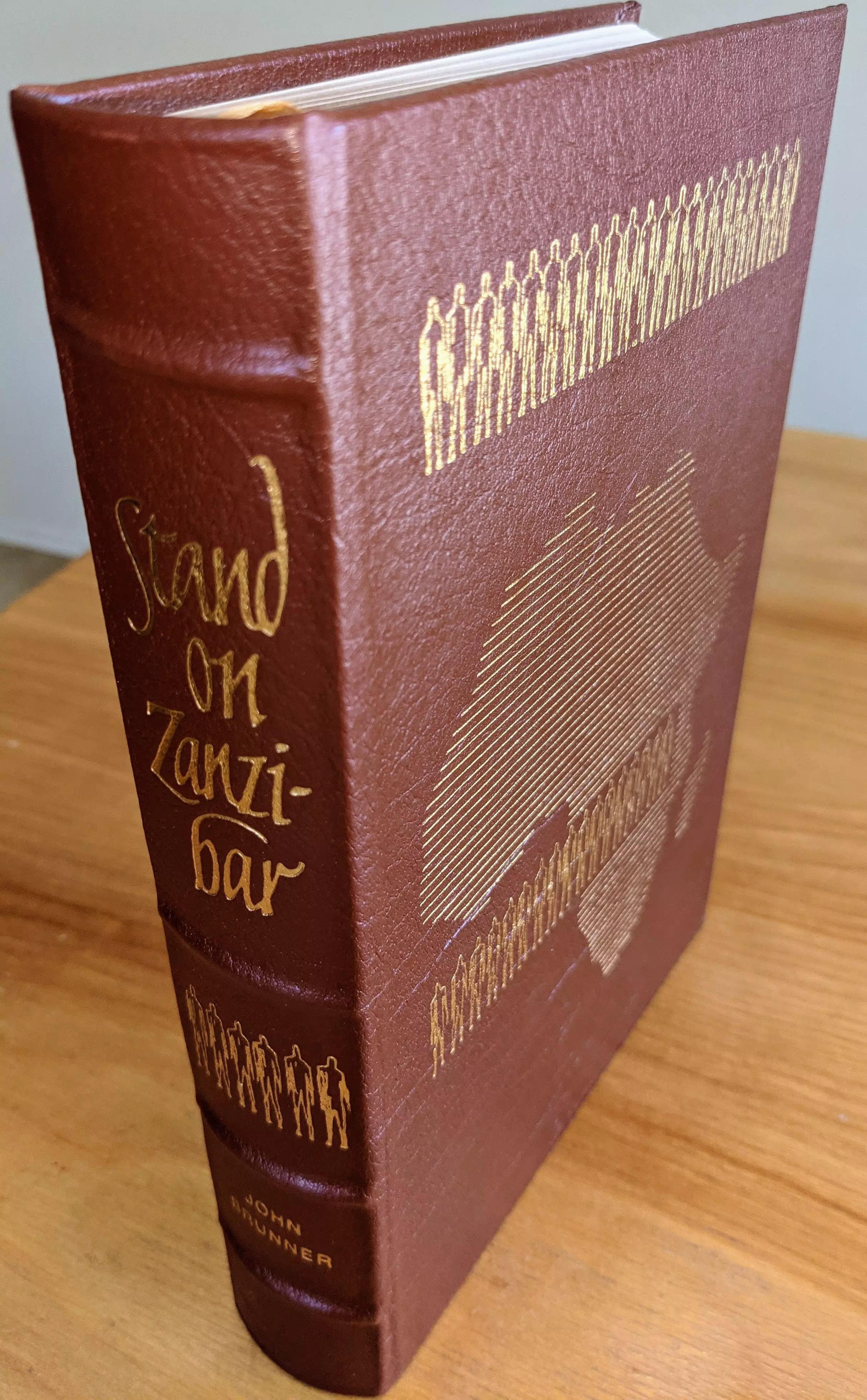 Pristine Collector's Edition of Stand on Zanzibar by John Brunner, part of the Masterpieces of Science Fiction Collection by The Easton Press. The book is single-owner, stored in a dust-free bookcase in a dry climate and is in exceptional, unused condition 
 - 
The full leather binding is a deep, rich brown, accented in 22kt gold. The elaborate cover artwork, created by the acclaimed Vincent DiFate, features several rows of stylized gold-outlined figures and a line-drawn map of Africa. The spine displays the book's title, 'Stand on Zanzibar,' in expressive gold script, flanked by lines of gold-embossed human silhouettes and the author's name in small capital gold print. The leather is thick, with raised, hubbed spine bands, and the book displays flawless craftsmanship 
 - 
Archival-quality paper is used throughout, with all page edges gilded in brilliant gold. Smyth sewn binding and concealed muslin joints reinforce the book's physical integrity, ensuring durability and a luxurious reading experience. Inside the front cover lies a pristine bookplate. The volume's immaculate preservation reflects careful single ownership. This collector's edition combines artistic, material, and literary value, resulting in a truly stunning and important item for aficionados of fine press science fiction
