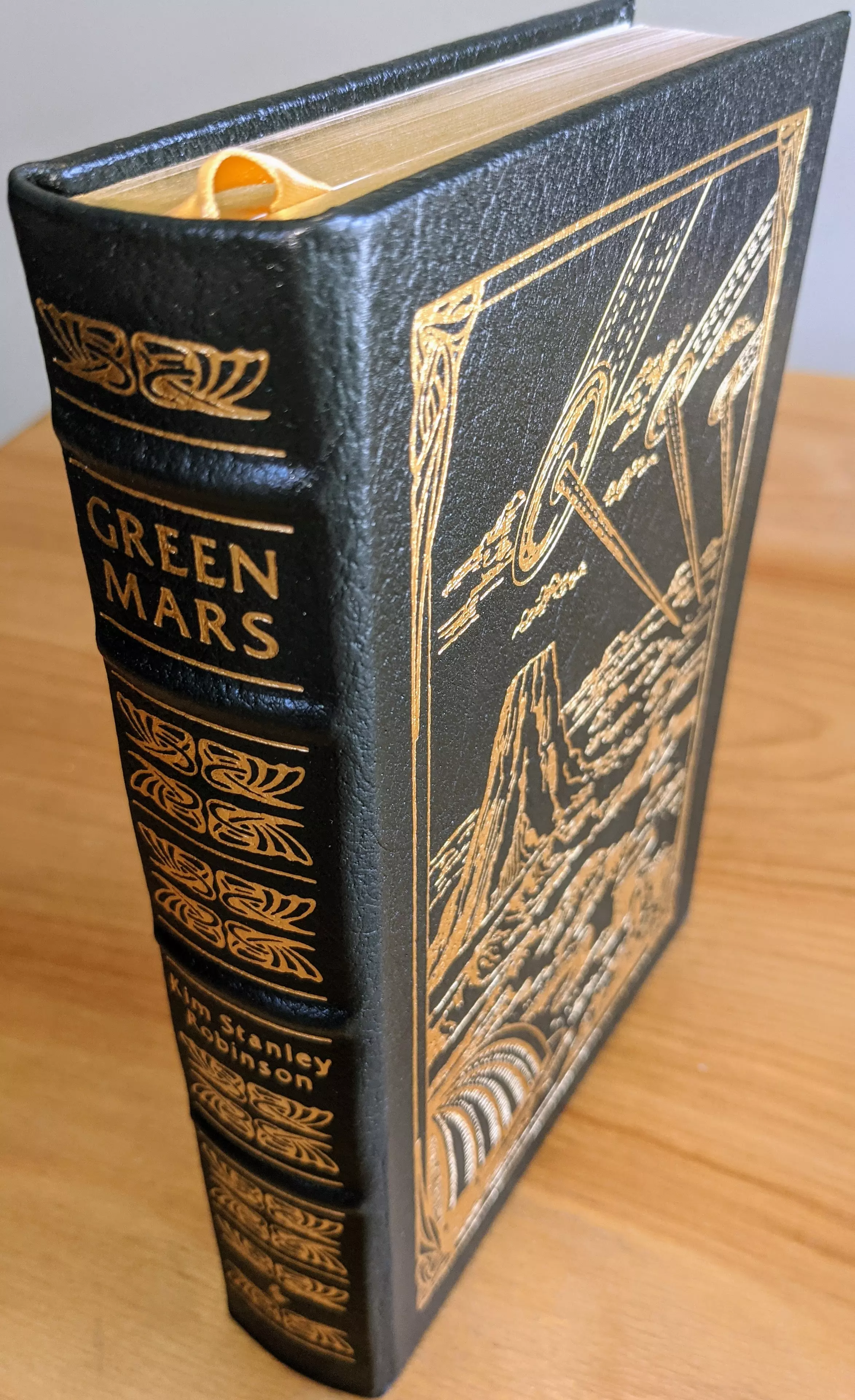 Luxurious collector's edition of Green Mars by Kim Stanley Robinson, part of The Easton Press's Masterpieces of Science Fiction collection. The book is bound in full deep dark green leather and features intricate gold accents. Its cover and spine are richly decorated with original artwork by Ron Walotsky, embossed in 22kt gold, showcasing a futuristic Martian landscape with dramatic imagery, including towering structures and celestial elements. The spine is hubbed, a hallmark of high-quality craftsmanship, with raised bands and detailed gold embellishments. Introduction by Pamela Sargent
 - 
The volume is printed on archival-quality acid-neutral paper designed for longevity, with 22k gold gilded edges that shimmer in the light. Smyth-sewn binding and concealed muslin joints ensure durability and flexibility, allowing the book to lay flat when opened. A satin ribbon bookmark in golden yellow adds a touch of elegance. Inside the front cover is a pristine bookplate, untouched and ready for personalization
 - 
This particular copy comes from a single-owner private collection, stored meticulously in dust-free bookcases within a dry climate to preserve its pristine condition. It has been exceptionally well-maintained and shows no signs of wear or damage, making it a stunning example of fine bookmaking for collectors and enthusiasts alike
