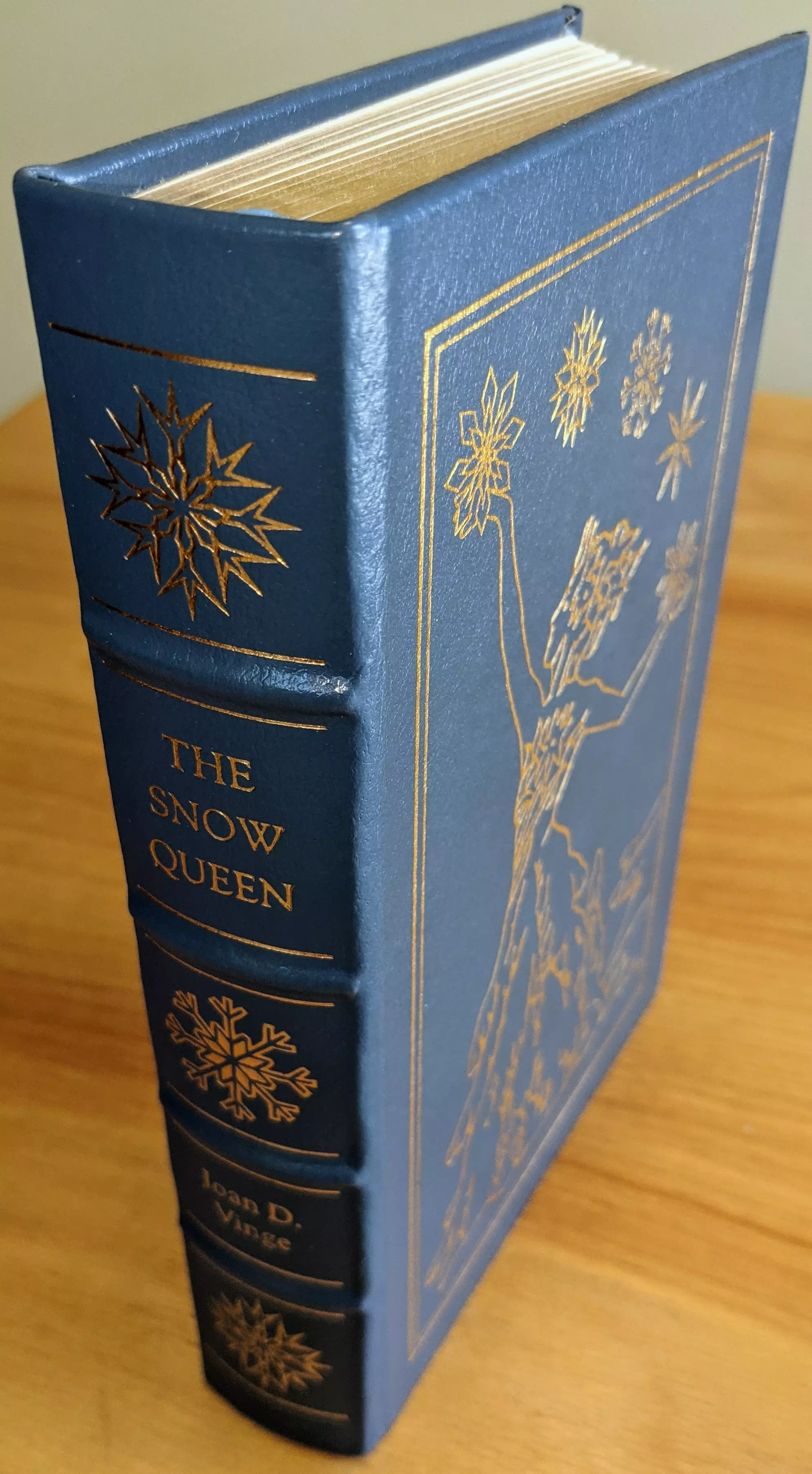 Stunning light blue leather-bound book club collector's edition of The Snow Queen by Joan D. Vinge, from the Masterpieces of Science Fiction Collection by The Easton Press (1990)
 - 
The cover is adorned with 22kt gold-embossed artwork by Pat Morrissey, featuring a dynamic depiction of snowflakes above a woman with a crown reaching for the sky. The scene is framed with elegant gold borders. The spine features the title The Snow Queen in bold gold serif font, alongside the author's name Joan D. Vinge and various large snowflakes in 22k gold
 - 
This edition is bound in full leather with raised hubbed spines. The book is printed on archival-quality acid-neutral paper with 22k gold gilded edges, combining aesthetic brilliance with preservation. Smyth-sewn binding and concealed muslin joints provide flexibility and long-lasting structural integrity
 - 
Maintained in pristine condition, this book has been carefully stored unread in dust-free bookcases within a dry climate as part of a single-owner private collection. Inside the front cover is a pristine, untouched bookplate
 - 
This edition also features an introduction by Greg Bear, offering insightful context. A masterpiece of literary craftsmanship and artistry, this volume is a perfect tribute to Joan D. Vinge and her novel The Snow Queen.